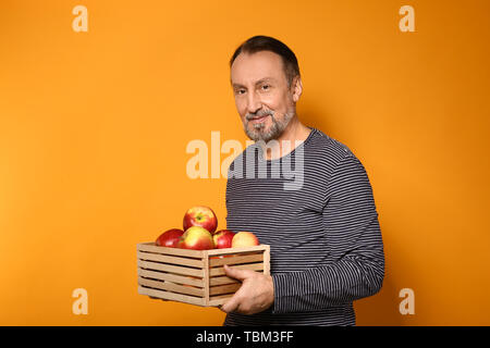 Portrait of handsome mature farmer with apples in box on color background Stock Photo