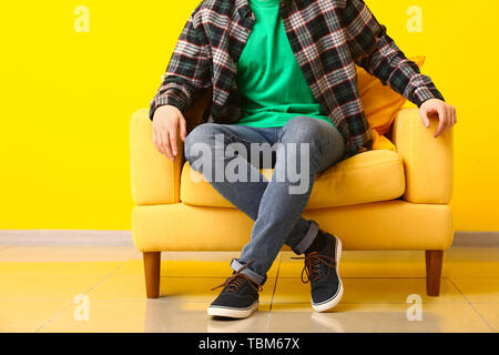 Stylish man in shoes sitting in armchair near color wall Stock Photo