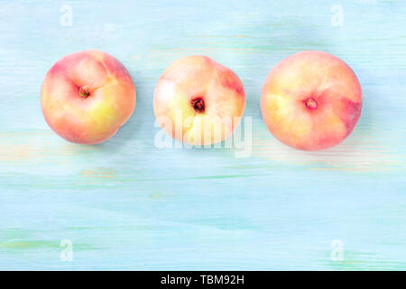 An overhead photo of vibrant organic flat saturn peaches, shot from the top on a teal background with a place for text Stock Photo