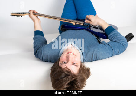 Happy young man lying back on sofa with guitar Stock Photo