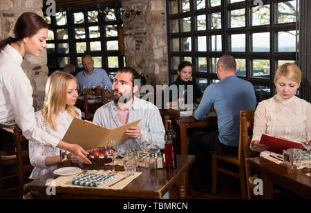 Guests of the country restaurant discuss menu with waitress Stock Photo