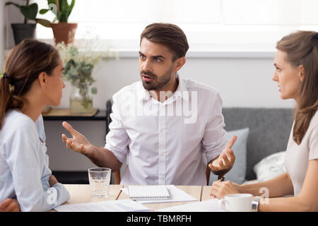 Angry businessman arguing with female subordinate at group business meeting Stock Photo