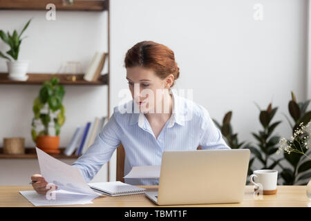 Concentrated serious young woman working with business document and laptop Stock Photo