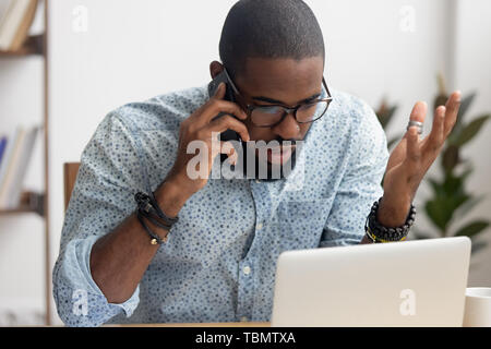 Angry mad african-american businessman talking on cellphone in office Stock Photo