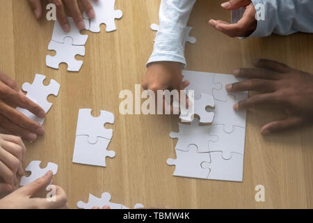 Top above close up view multiracial human hands assembling puzzle Stock Photo