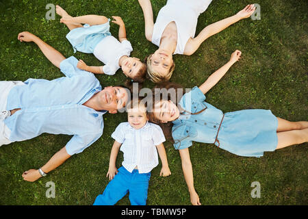 happy playful family lying on the grass outdoors. parents with children in the summer. Mom, dad and kids Stock Photo