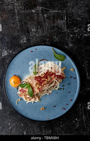 Classic pasta carbonara with yolk on a plate. Pasta laid out on a blue plate on a dark background. Concept of Italian cuisine, beautiful serving Stock Photo
