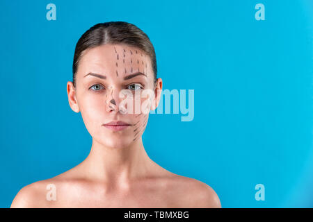 Beautician draw correction lines on woman face. Before plastic surgery operetion. Isolated on blue
