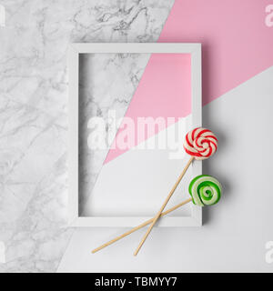 Flat lay white photo frame and two colorful lollipops on a white, pink and marble background. Stock Photo