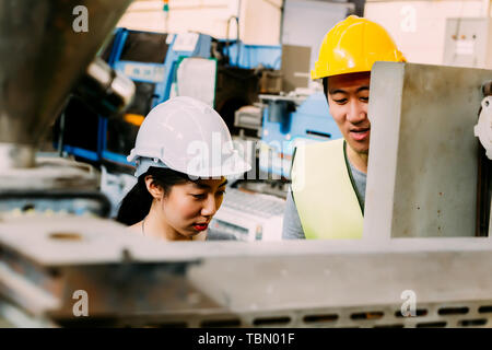 Young Asian male factory engineering manager teaching female mechanic trainee for job training and apprentice Stock Photo
