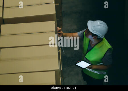 Top view of young warehouse worker man with safety hard hat is checking order details with a digital tablet at inventory room Stock Photo