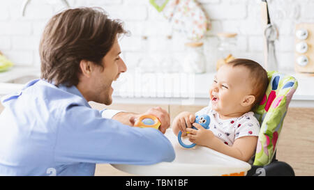 Millennial man laughing with his baby son in kitchen Stock Photo