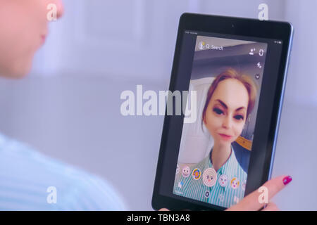 Woman using Snapchat multimedia messaging app with face mask on tablet Stock Photo