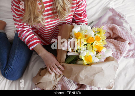 Woman with bouquet of beautiful flowers sitting on bed Stock Photo