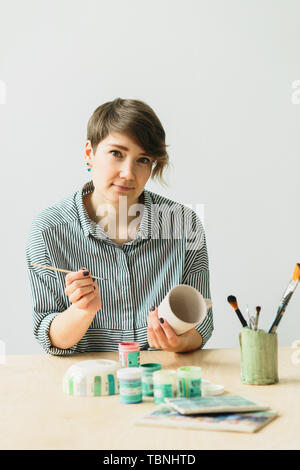 the pottery woman holds in hands a mug to paint the ornament, handmade ceramic Stock Photo