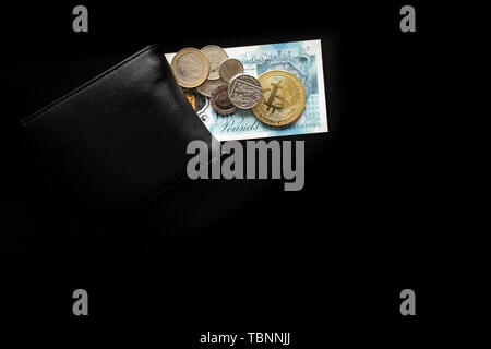 A physical bitcoin sits on top of English Pounds next to a wallet Stock Photo