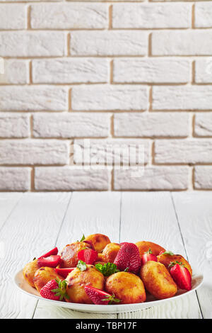 close-up of cottage cheese donuts served with strawberries on a plate on a wooden table with a brick wall at the background, empty space Stock Photo