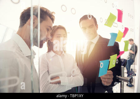 Happy girl works with colleagues in office with post it notes in foreground. Concept of teamwork and partnership. Stock Photo