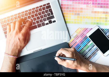 designer hand working with new modern computer laptop and pro digital tablet with sample color board on white desk Stock Photo