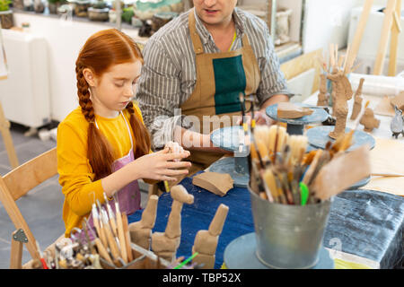 Pupil and teacher. Red-haired beautiful cute pupil and her art teacher modeling clay figures Stock Photo