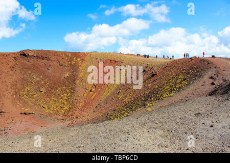 People walking around the colorful crater in Silvestri craters on Mount Etna in Sicily, Italy. The stunning volcanic landscape is a popular hiking spot. Stock Photo