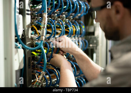 Close-up of busy server support specialist inserting cables into hubs and examining connectivity while repairing supercomputer Stock Photo