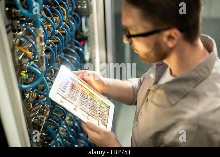Close-up of concentrated man in shirt standing by mainframe and using digital tablet to check connectivity in datacenter room Stock Photo