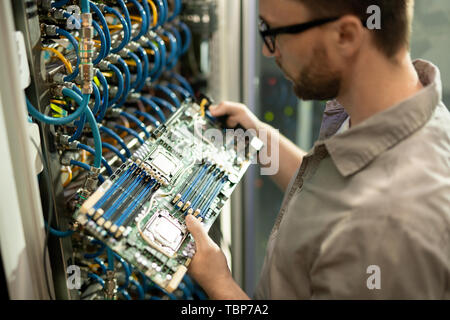 Close-up of serious bearded IT support specialist standing by cabinet of mainframe and examining motherboard of server Stock Photo