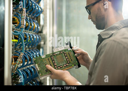 Serious skilled young IT engineer standing at server of database storage and inspecting supercomputer motherboard Stock Photo