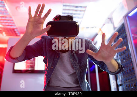 Serious curious young middle-eastern innovation scientist gesturing hands while using virtual reality simulator in database storage room Stock Photo
