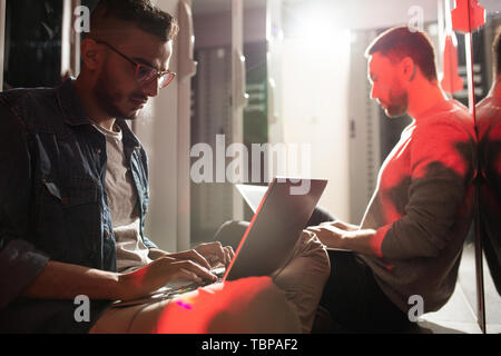Serious concentrated young multi-ethnic programmers sitting on floor in server room and using laptops while doing research of networking connectivity Stock Photo