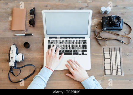 High angle view of unrecognizable photographer sitting at wooden table and checking shoots on laptop, knolling image Stock Photo