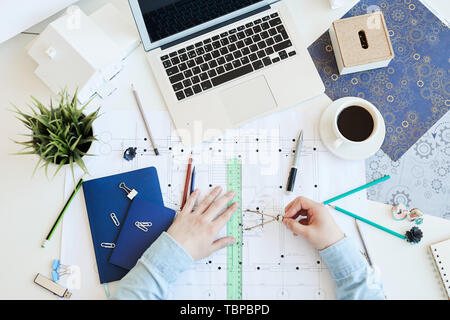 High angle view of unrecognizable architect in casual shirt sitting at table and using pair of compasses while working on housing plan Stock Photo