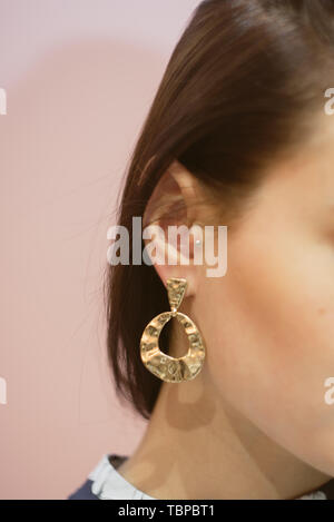 round gold earrings on the ear of a brunette on a pink pastel background. Costume jewelry on the girl. Stock Photo