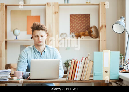 Serious concentrated young project manager focused on work using modern laptop and viewing data in modern business studio Stock Photo