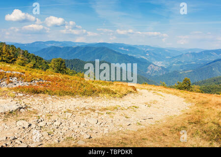 gravel road through the mountain meadow.  beautiful summer scenery with clouds on a blue sky. wonderful landscape with village in the distant valley.  Stock Photo
