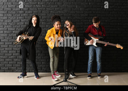 Band of teenage musicians playing against dark wall Stock Photo