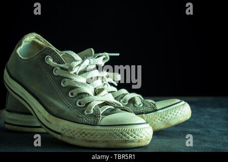 Dirty sneaker in darkness. Closeup old sneaker on black cement floor. Copy space for text. Concept of traveling. Stock Photo