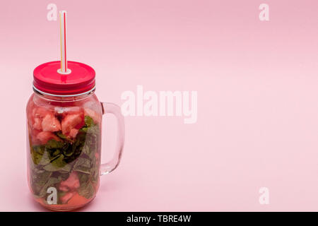 Jar of cold fresh lemonade with piece of watermelon and drinking straws on pink background. Stock Photo
