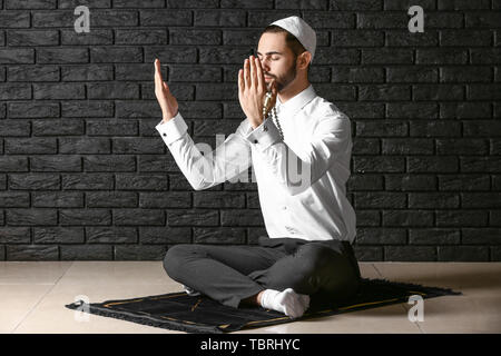 Young Muslim man praying against dark brick wall Stock Photo