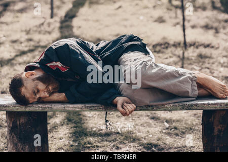 Poor homeless man lying on bench outdoors Stock Photo