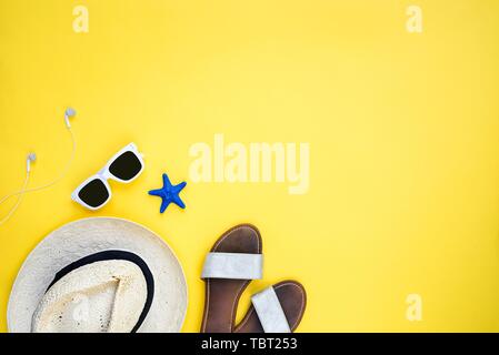 Summer vacation accessories. Straw hat, white sunglasses, earphones and flip-flops over yellow background. Copy space, flat lay. Stock Photo