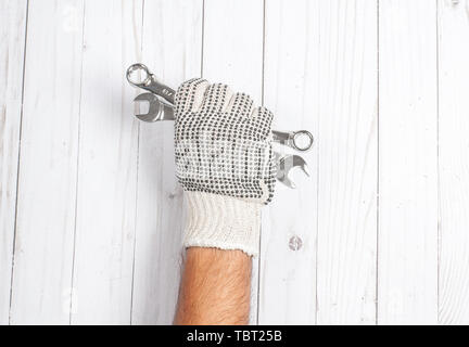 Tool. Hand in glove is holding wrenches isolated on white wooden background. Stock Photo