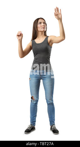 Young woman in gray top and blue jeans standing, one hand in 'pinch' gesture and other raised as if touching invisible glass isolated on white Stock Photo