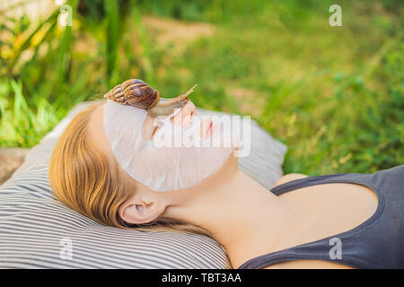 Young woman makes a face mask with snail mucus. Snail crawling on a face mask Stock Photo