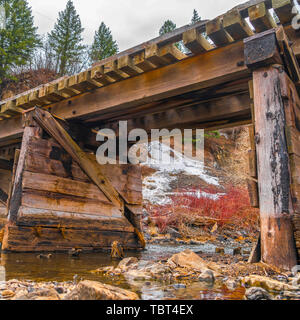 Square Rustic wooden bridge crossing over a rocky stream with clear shallow water Stock Photo