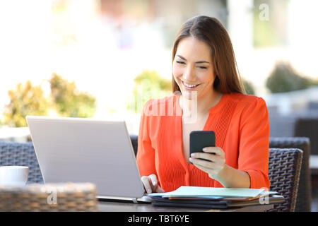 Happy entrepreneur using multiple electronic devices sitting in a coffee shop terrace Stock Photo