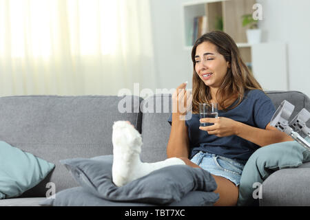 Disabled woman complaining crying taking pill sitting on a couch at home Stock Photo
