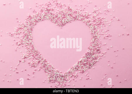 Pink and white pearly cake sprinkles shaped in a heart shape with empty space for text in the centre of heart - Sprinkles on pink background - top vie Stock Photo