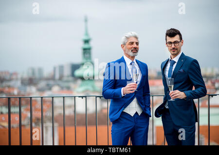 Businessmen with champagne standing outdoors on roof terrace in city. Stock Photo